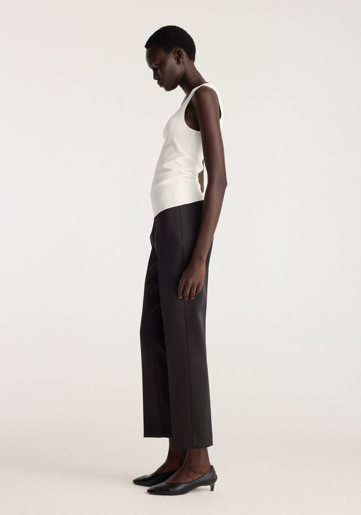 Bustier shaped knitted top | optic white shown on a model with wide leg black trousers and pointed black heels in a minimalist studio