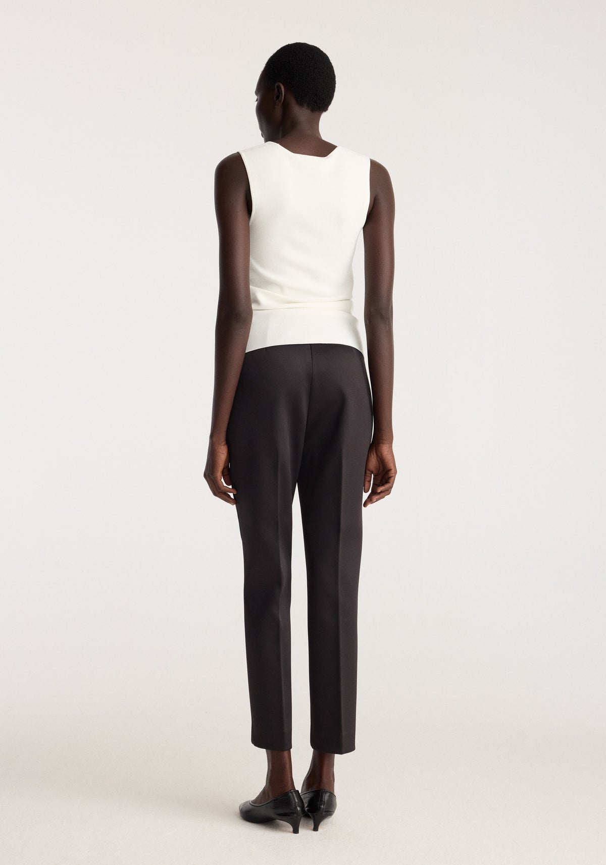 Back view of model wearing Bustier shaped knitted top | optic white with dark tailored trousers and black heels