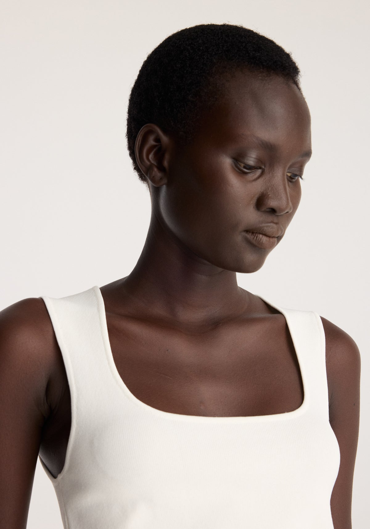 Bustier shaped knitted top | optic white worn by a model with a square neckline and wide shoulder straps in a close up studio portrait