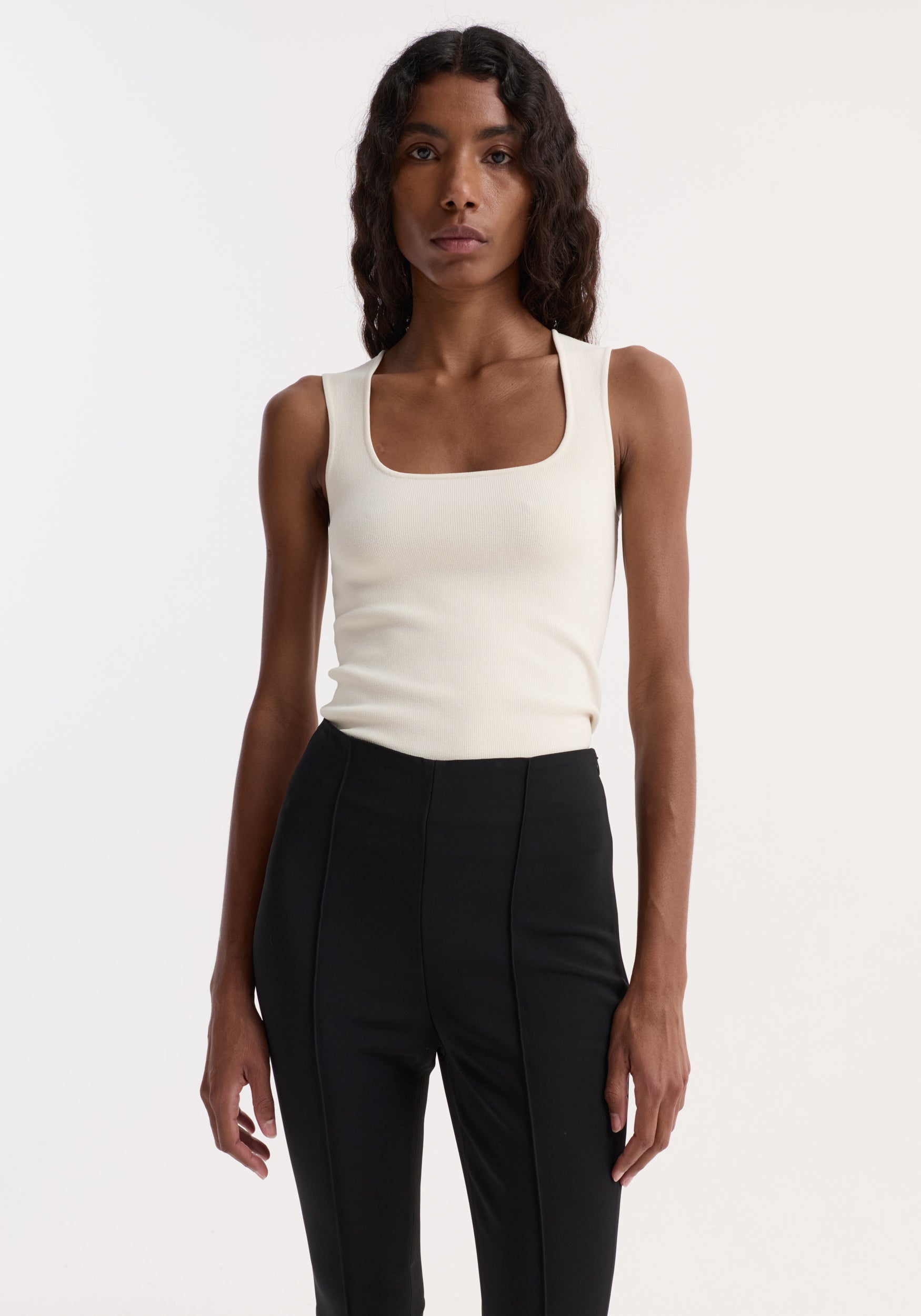 Woman wearing Bustier shaped knitted top | off white paired with black fitted pants against a plain white background.