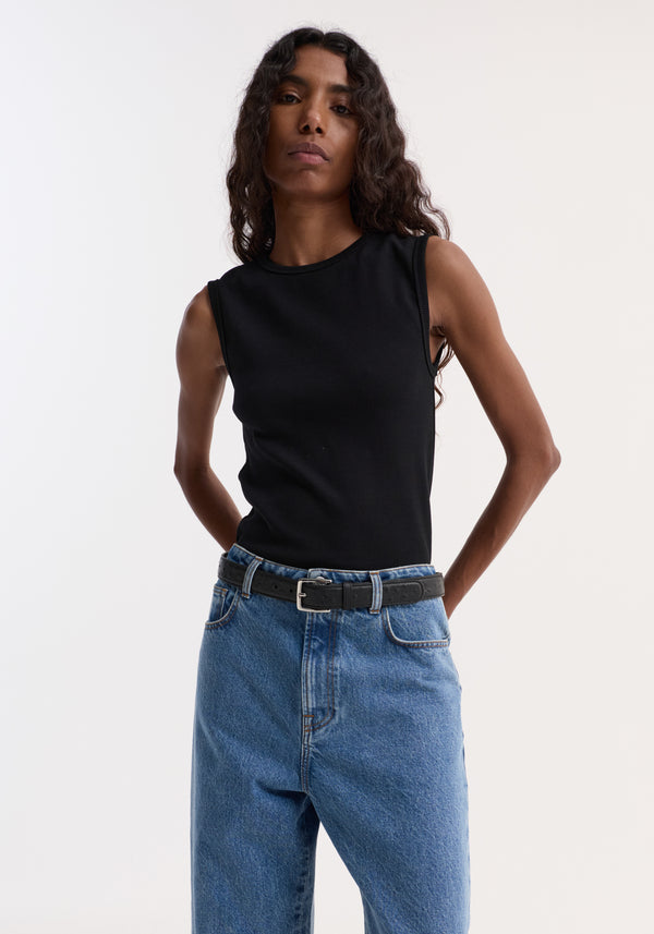 Person wearing Dense rib tank top in black, styled with high-waisted blue jeans and a belt, showcasing its fitted, ribbed texture and versatile, comfortable design.