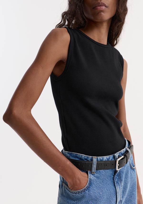 Dense rib tank top in black, fitted and sleeveless, worn with medium-wash jeans and a black belt. Made from 95% organic cotton, 5% elastane.