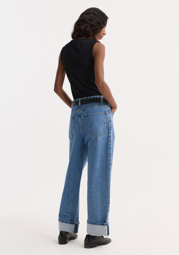 Person in a Dense rib tank top | black, showcasing its fitted design, paired with high-waisted jeans and black lace-up shoes, hands in back pockets.
