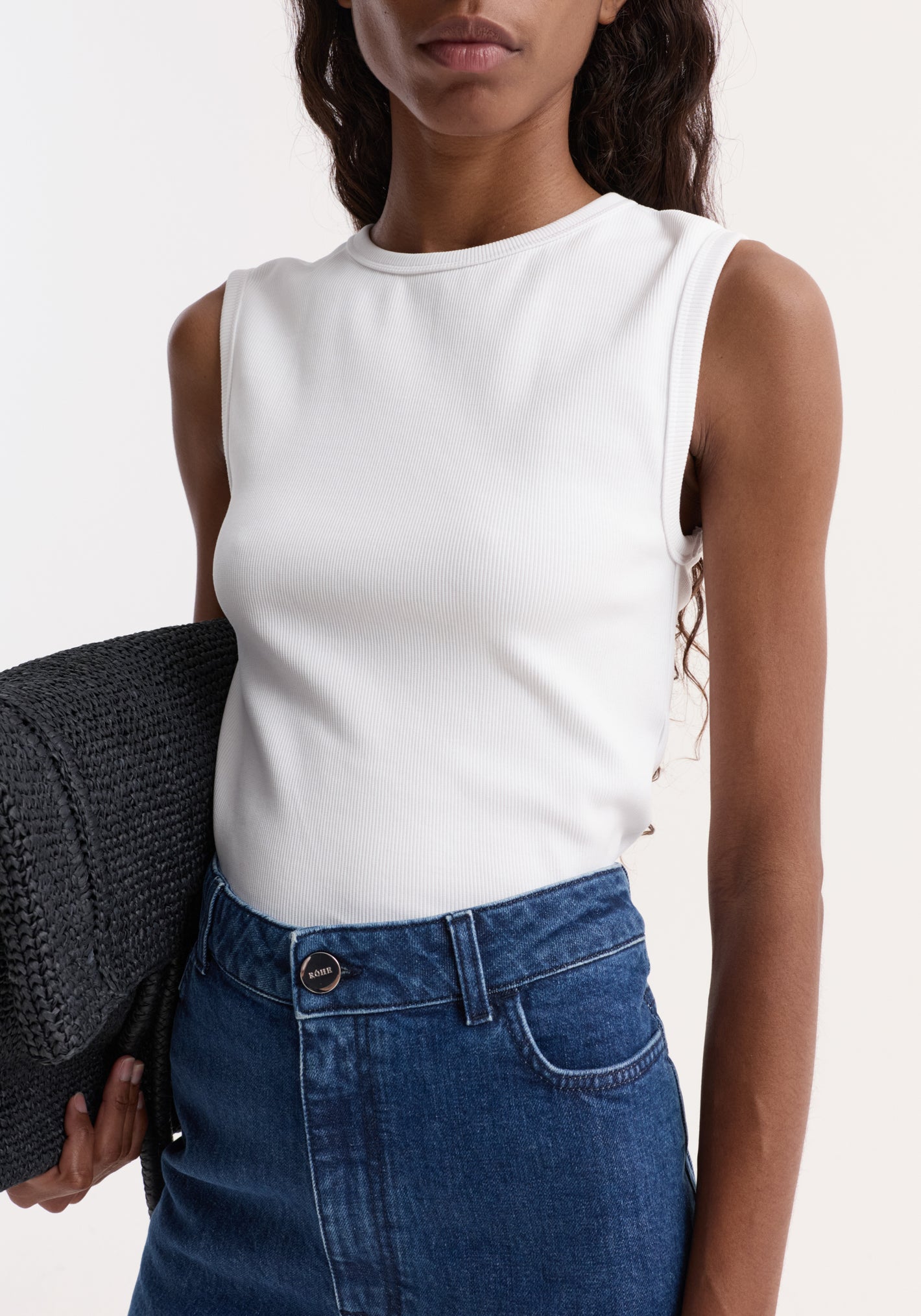Dense rib tank top in optic white, worn tucked into high-waisted denim. Made from organic cotton and elastane, offering comfort and versatility.