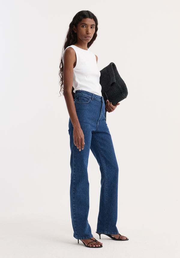 Model wearing Dense rib tank top in optic white, paired with blue jeans and black heeled sandals, holding a black sweater or clutch, against a plain background.
