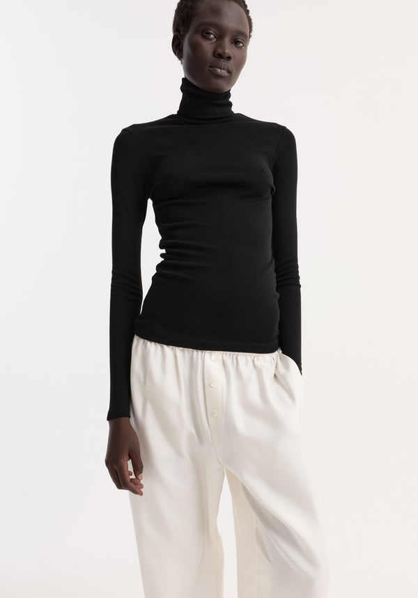 Fine merino turtleneck | black: Model wears a slim-fit, long-sleeve turtleneck in pure merino wool, paired with high-waisted trousers, showcasing minimalist style.