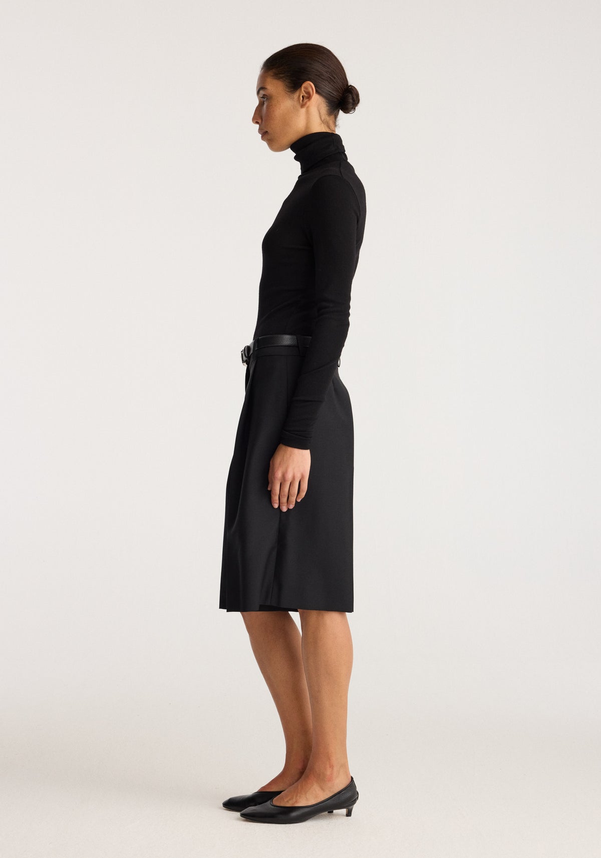 Fine merino turtleneck | black shown on a model in side profile with a high neck and long sleeves paired with a black skirt and heels