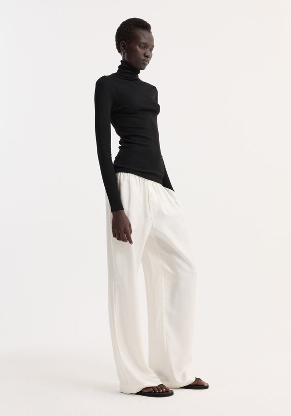 Model wearing Fine merino turtleneck in black, showcasing its fitted silhouette with long sleeves, paired with high-waisted, wide-leg trousers for a minimalist look.