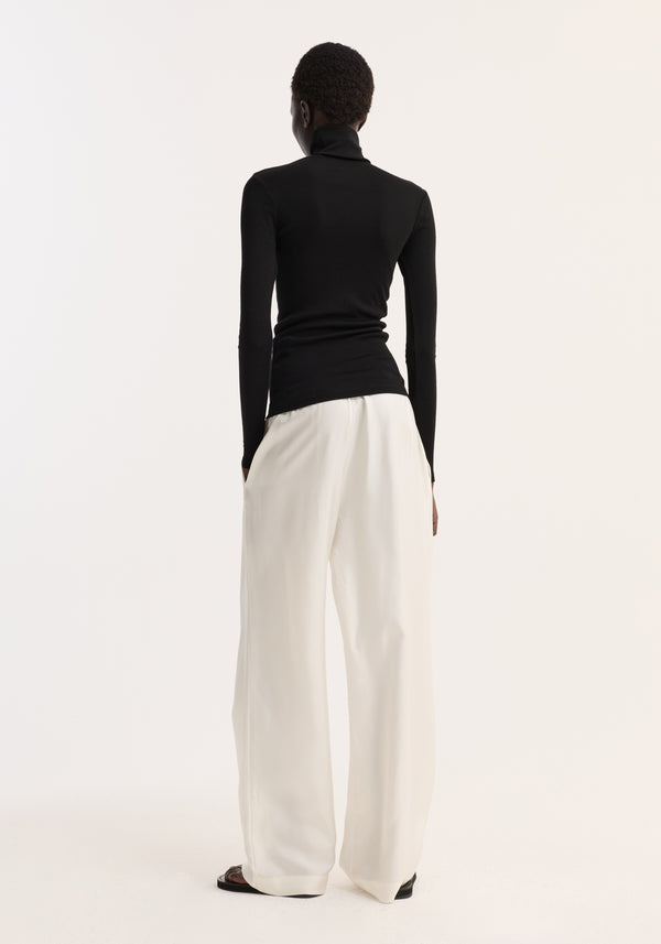 Fine merino turtleneck | black: A person wears a fitted black turtleneck made from pure merino wool, styled with wide-leg trousers, viewed from the back.