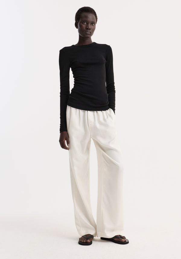 Model in Fine merino long sleeve | black, showcasing crew neck and fitted silhouette, paired with high-waisted trousers and flat sandals for a minimalist look.