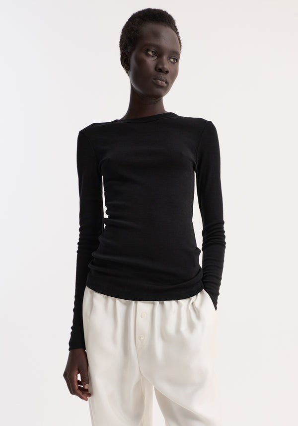 Fine merino long sleeve in black, worn by a tall woman with a fitted silhouette and crew neck, paired with high-waisted white trousers in a minimalist setting.