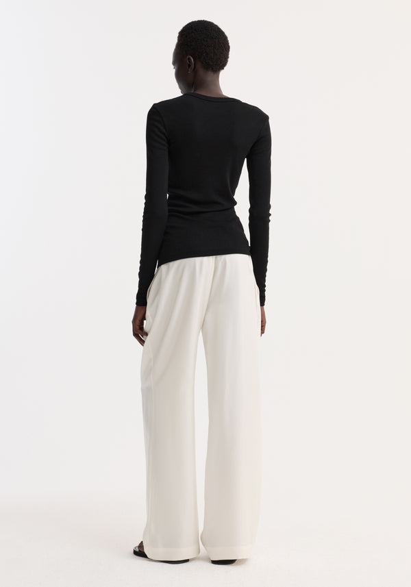 Fine merino long sleeve in black, crew neck, fitted silhouette, worn by model in high-waisted trousers, showcasing minimalist style against a white backdrop.