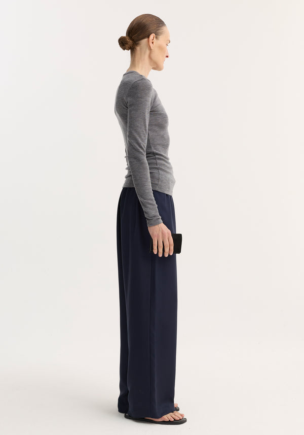Person in a slim-fitting Fine Merino Long Sleeve in mid grey melange, tucked into navy wide-leg trousers, holding a black clutch, styled minimally.