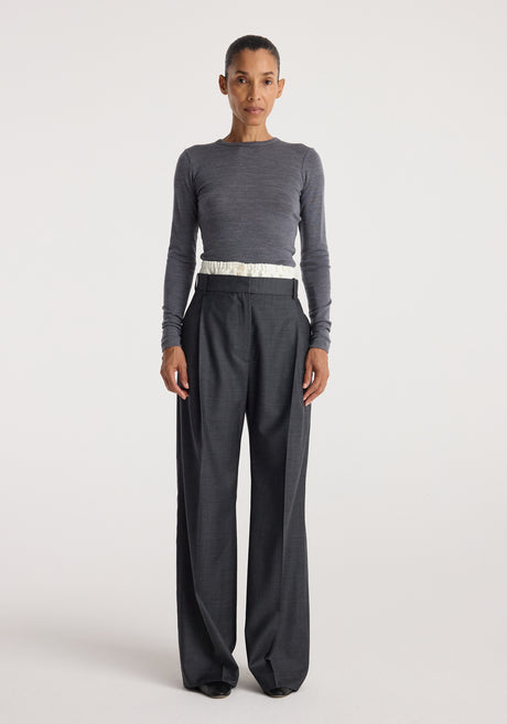Woman wearing a fitted fine merino long sleeve | mid grey melange top paired with loose dark grey trousers against a plain white background.