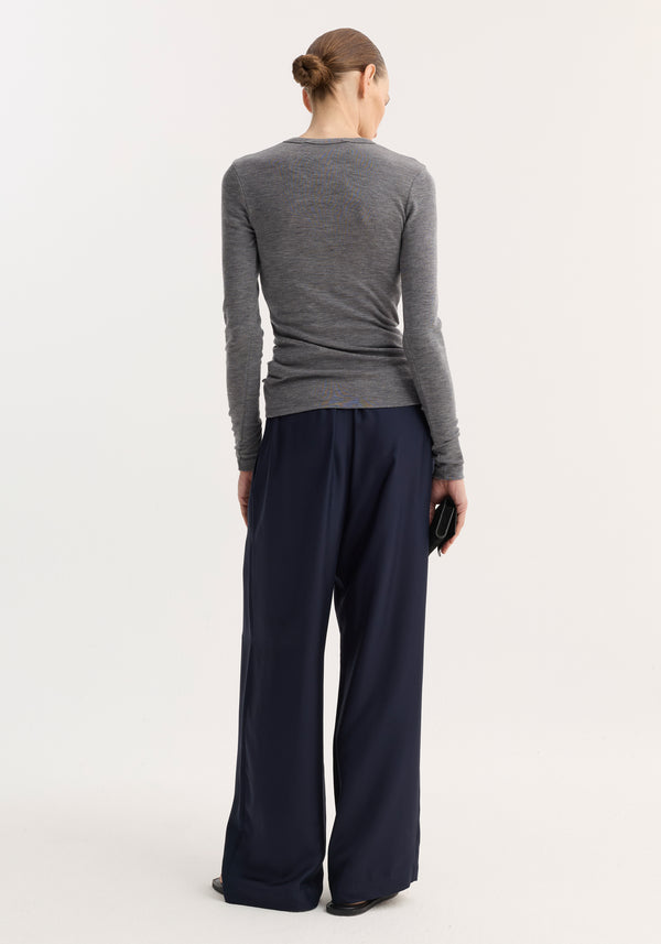 Model in a fitted Fine merino long sleeve in mid grey melange, tucked into wide-leg navy trousers, holding a black clutch, showcasing minimalist style.