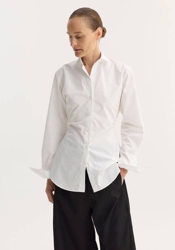 Person wearing the Poplin shaped shirt in optic white, featuring a relaxed hourglass fit, button-down design, and crafted from light cotton poplin, with unbuttoned cuffs.