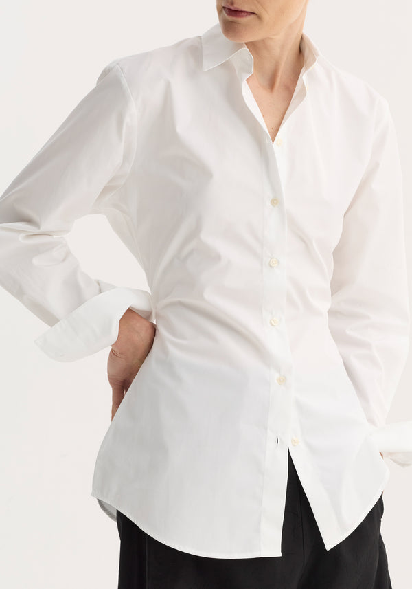 Model wearing Poplin shaped shirt in optic white with point collar and mother-of-pearl buttons, relaxed fit. Visible dark skirt or trousers.