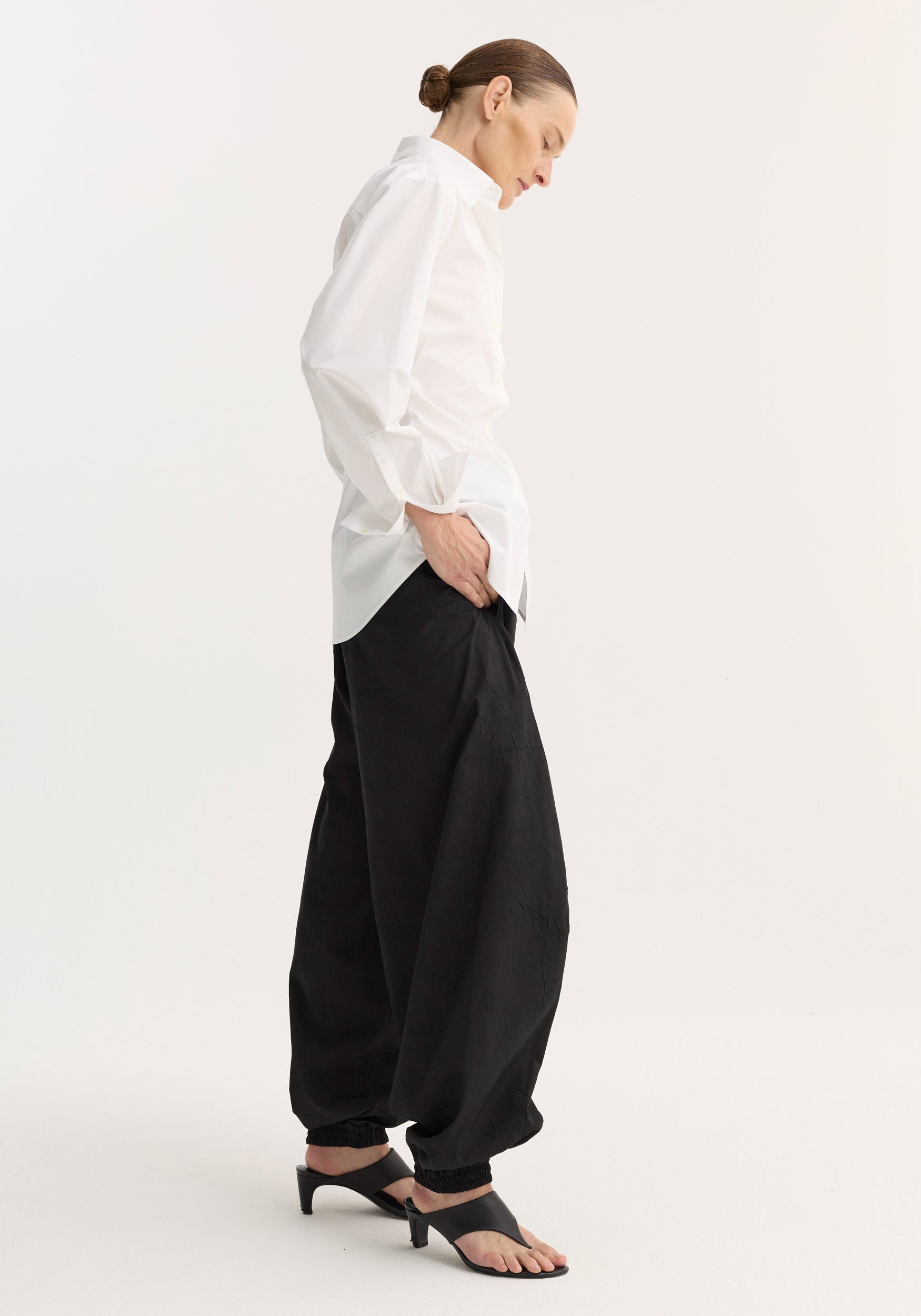 Model wearing Poplin shaped shirt | optic white, featuring a relaxed hourglass fit, untucked, paired with loose black pants and black slide sandals.