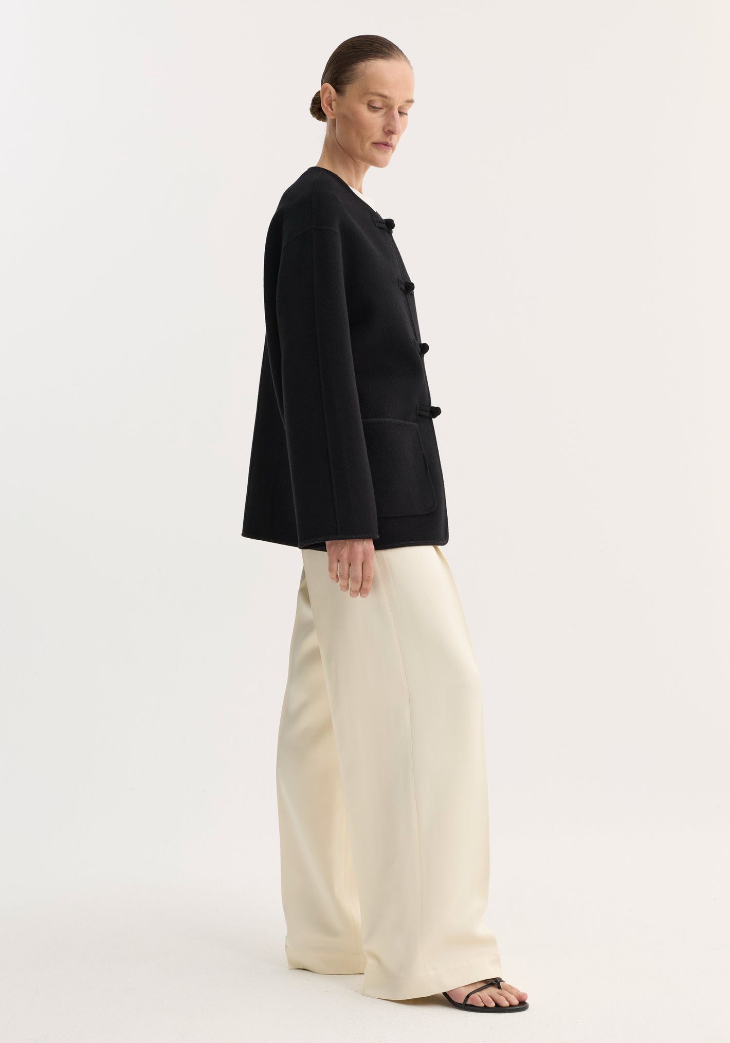 Woman wearing Róhe 'Marie' mandarin double-faced wool jacket with embroidered edges, patch pockets, and pankou closure, paired with wide-leg trousers and sandals.