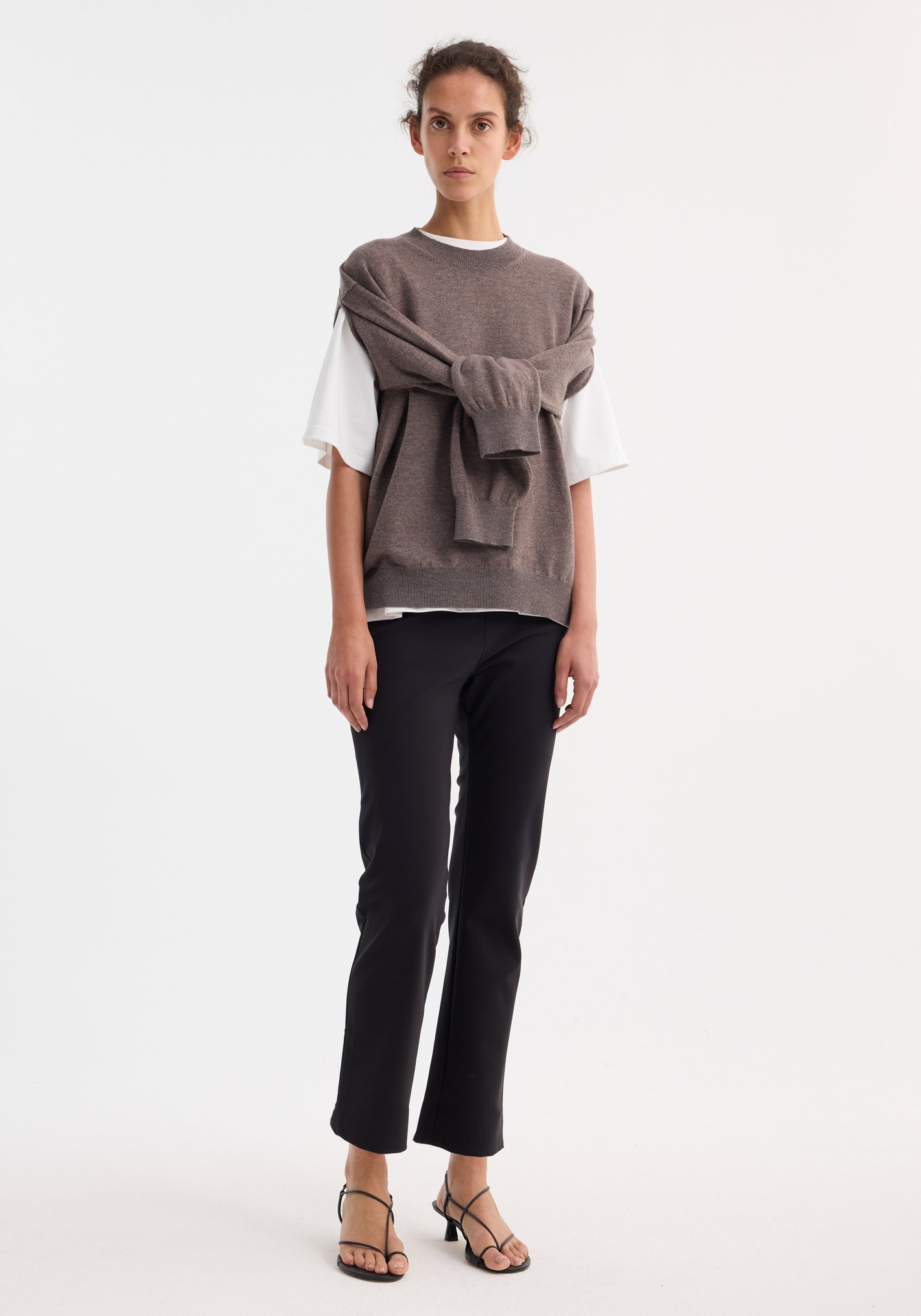 Woman wearing Cigarette scuba trousers | black, showcasing tailored ankle-length fit, paired with a white T-shirt and taupe knitwear, styled with black strappy heeled sandals.