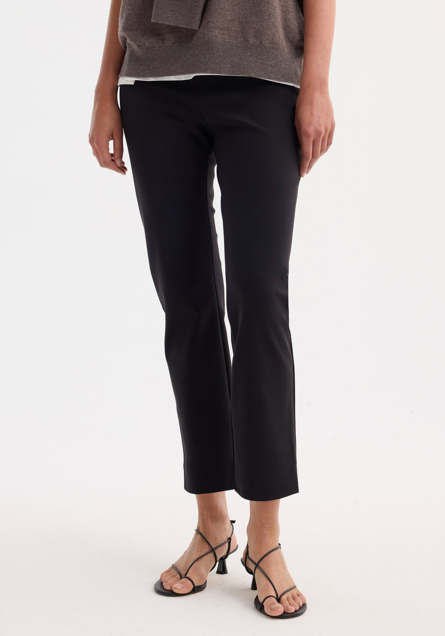 Cigarette scuba trousers in black, slim-fit and ankle-length, shown with strappy black high-heeled sandals, illustrating sleek tailoring and modern versatility.