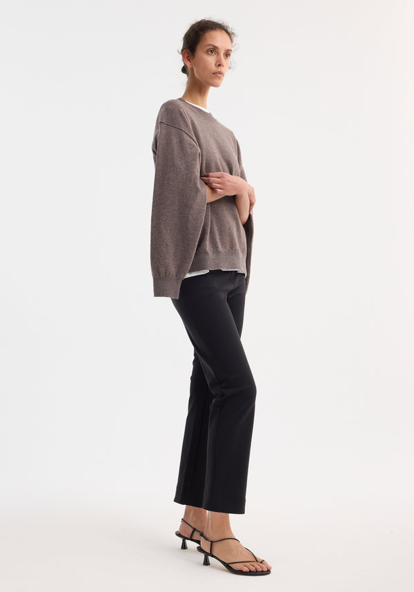 Model in black cigarette scuba trousers with a sleek, tailored ankle-length design, paired with a taupe sweater and low-heel sandals, exuding modern elegance.