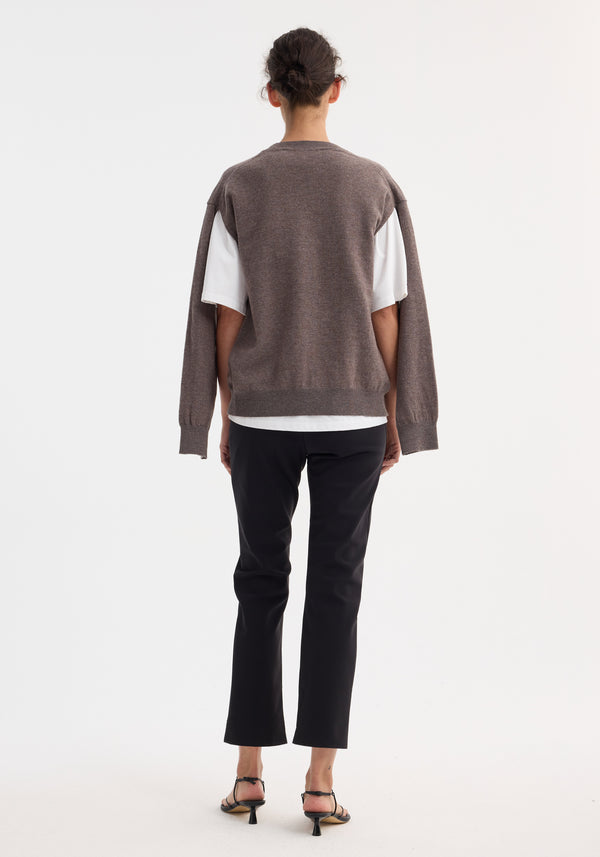 Model wearing cigarette scuba trousers in black with a tailored, ankle-length fit, paired with a white T-shirt and brownish-taupe knit sweater.