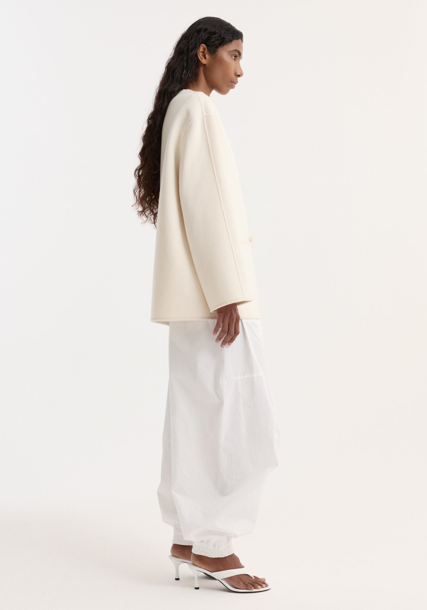 Model in an off-white double-faced wool pankou jacket with embroidered edges and patch pockets, paired with voluminous pants and minimalist heeled sandals.