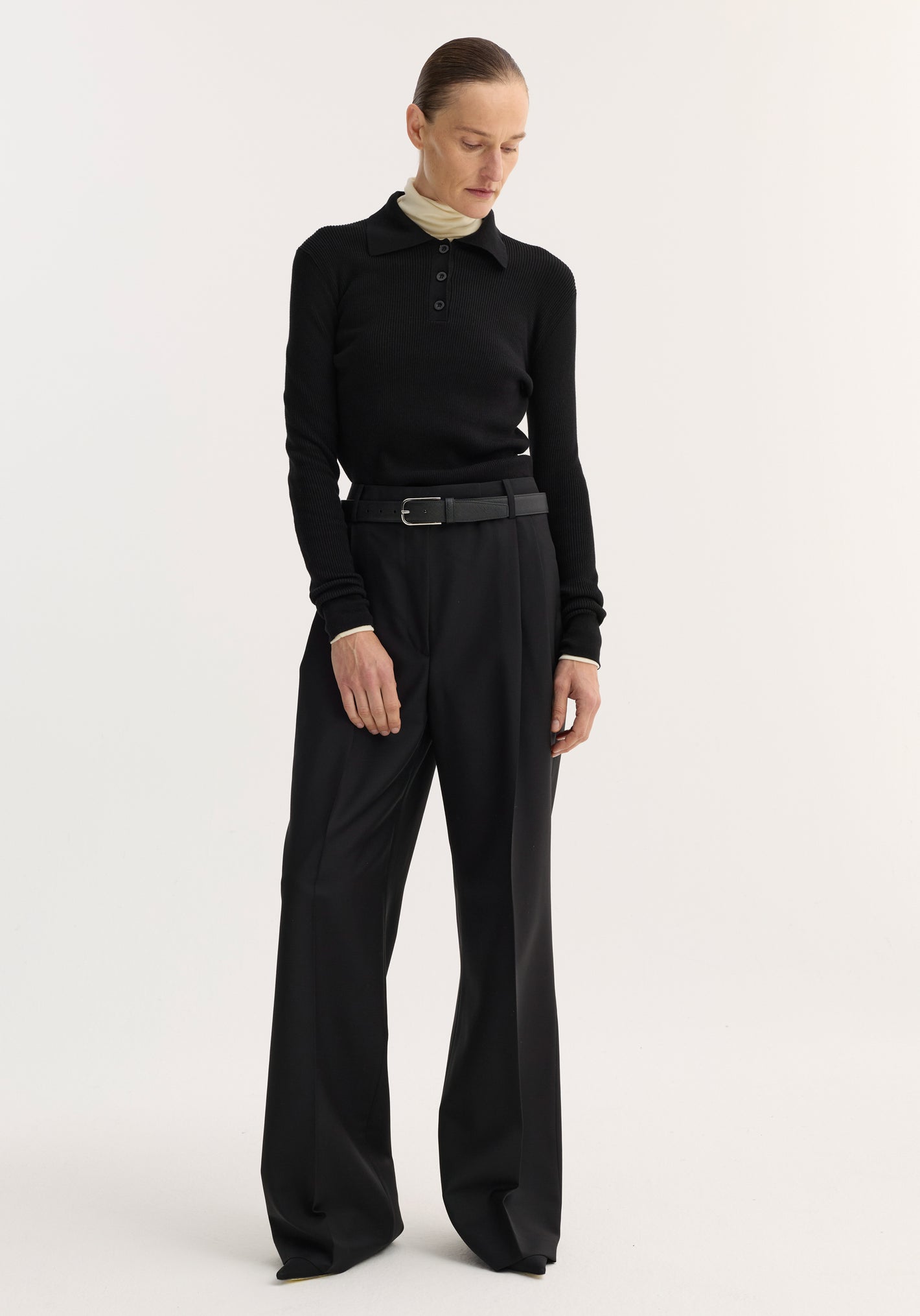 Rib knitted polo | black: A sleek, ribbed black polo featuring a fitted silhouette, long sleeves, and a three-button placket, styled with high-waisted wide-leg trousers.