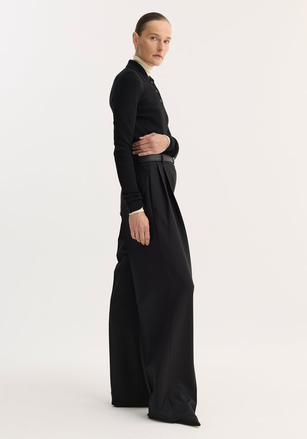 Model wearing Rib knitted polo | black, featuring a slim fit, long sleeves, and three-button polo neckline, paired with wide-leg trousers and sleek hairstyle.