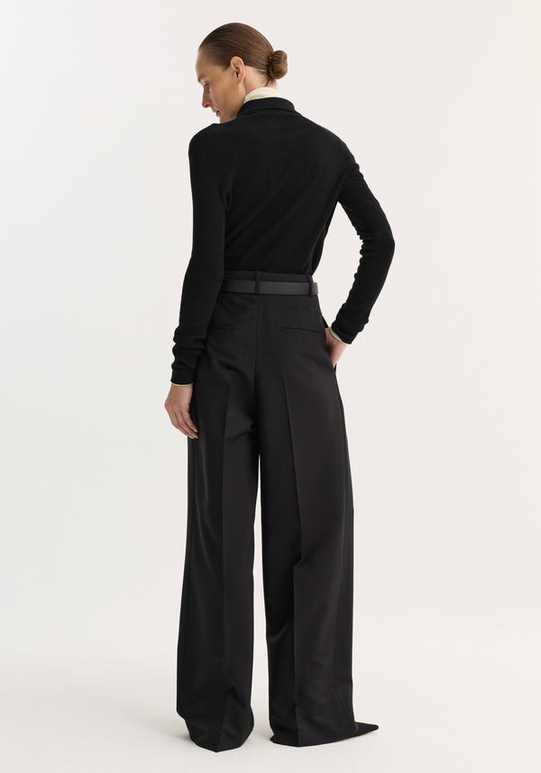 Rib knitted polo | black: Rear view of model in fitted black ribbed polo top with long sleeves, paired with high-waisted wide-leg trousers, emphasizing the top's silhouette.