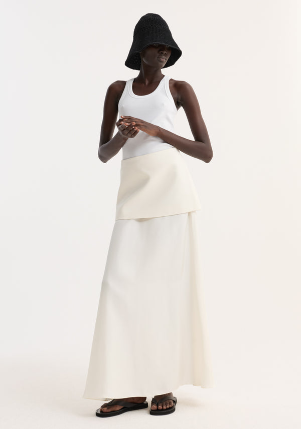 Model in a white tank top and Integrated fluid silk skirt | cream, with a high waist and sculptural silhouette, wearing a black crocheted bucket hat.