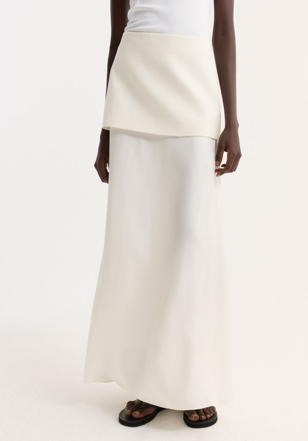 Integrated fluid silk skirt in cream, featuring a high waist and sculptural silhouette, paired with black sandals, highlighting its elegant, flowing design.
