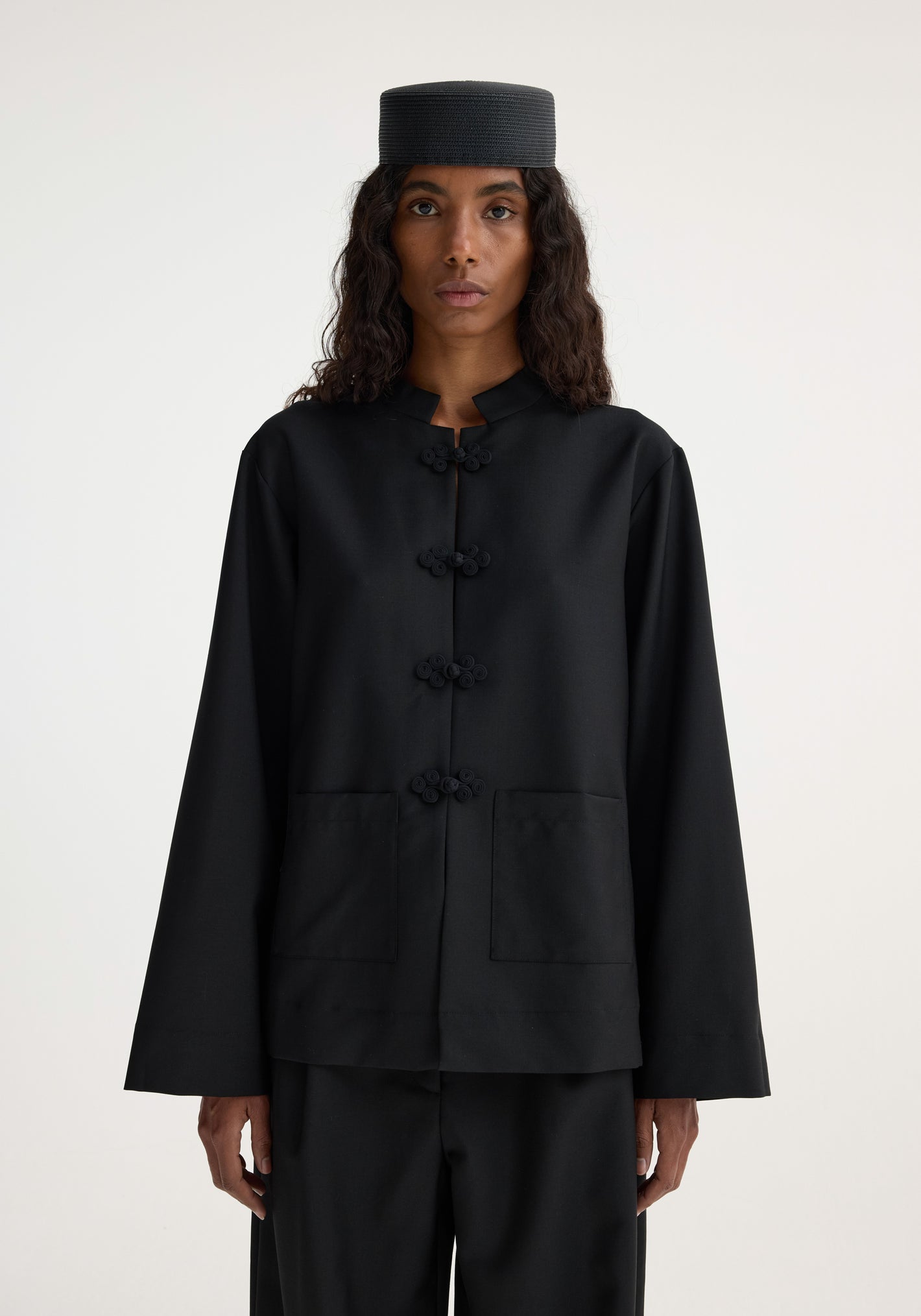 Person in a minimalist Mandarin jacket | black with pankou closure, patch pockets, and matching trousers, showcasing a sophisticated and timeless design.