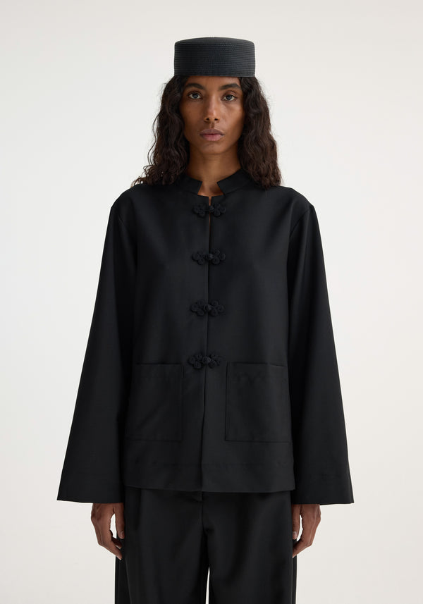 Person in a minimalist Mandarin jacket | black with pankou closure, patch pockets, and matching trousers, showcasing a sophisticated and timeless design.