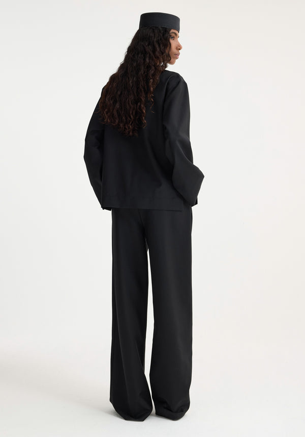 Model in profile wearing Róhe's Mandarin jacket in black, showcasing the loose-cut style and distinctive mandarin pankou closure, with long, wavy hair cascading down.