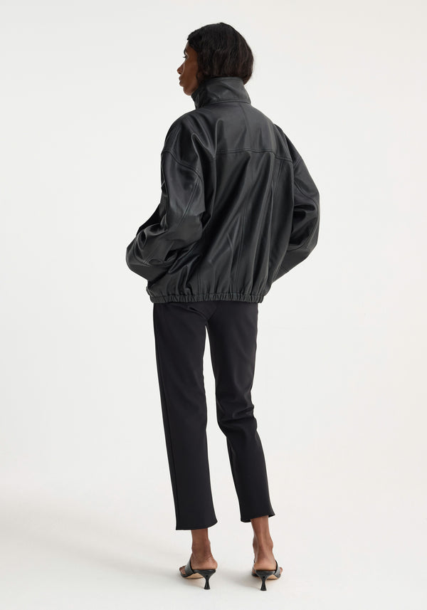 Model in oversized Reinvented leather jacket | black, showcasing its high stand collar, elasticized hem, and snap button details, with back turned slightly to camera.