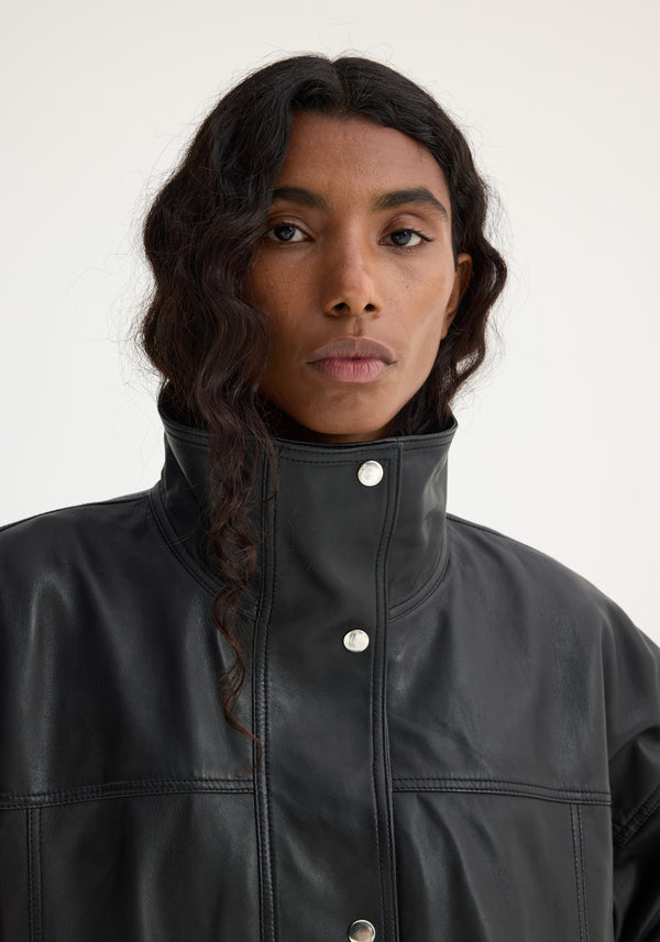Reinvented leather jacket | black, featuring a high-collared silhouette with silver snap buttons and stitched paneling, worn by a model with long, dark wavy hair.