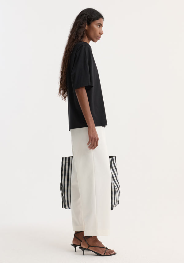 Model in Oversized cotton t-shirt, black, with a relaxed fit, dropped shoulders, and crew neck, paired with wide-leg trousers and striped tote.