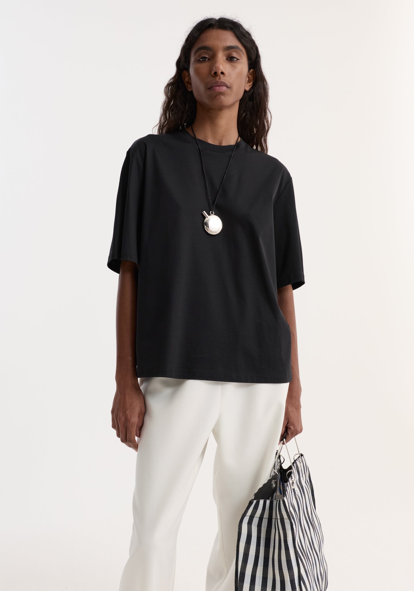 Model wearing a Silver perfume bottle necklace on a black cord, featuring a sterling silver design, paired with a minimalist black T-shirt and white trousers.
