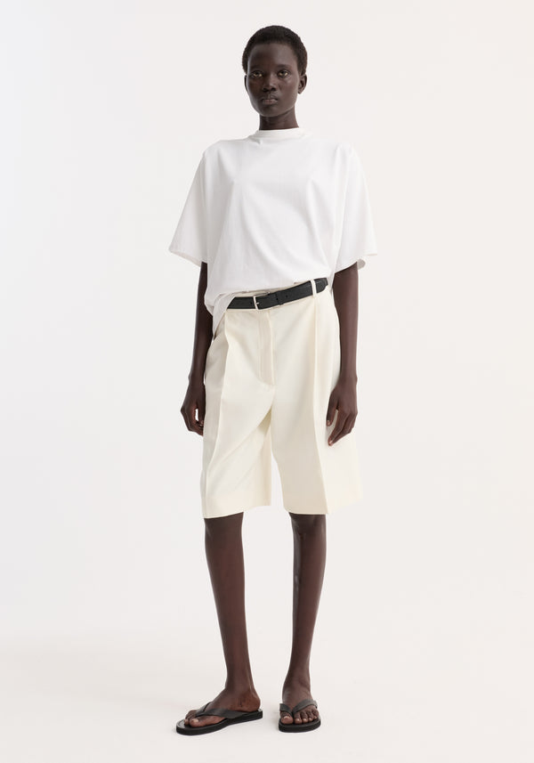 Model wearing an Oversized cotton t-shirt | optic white with high-waisted shorts, black leather belt, and black thong sandals, showcasing a relaxed, polished style.