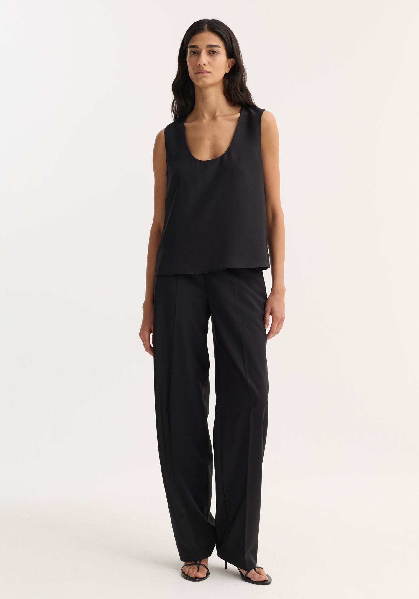 Model wearing Scoop-neck silk top | black, featuring a wide scoop neckline and loose fit, paired with high-waisted trousers and strappy sandals.