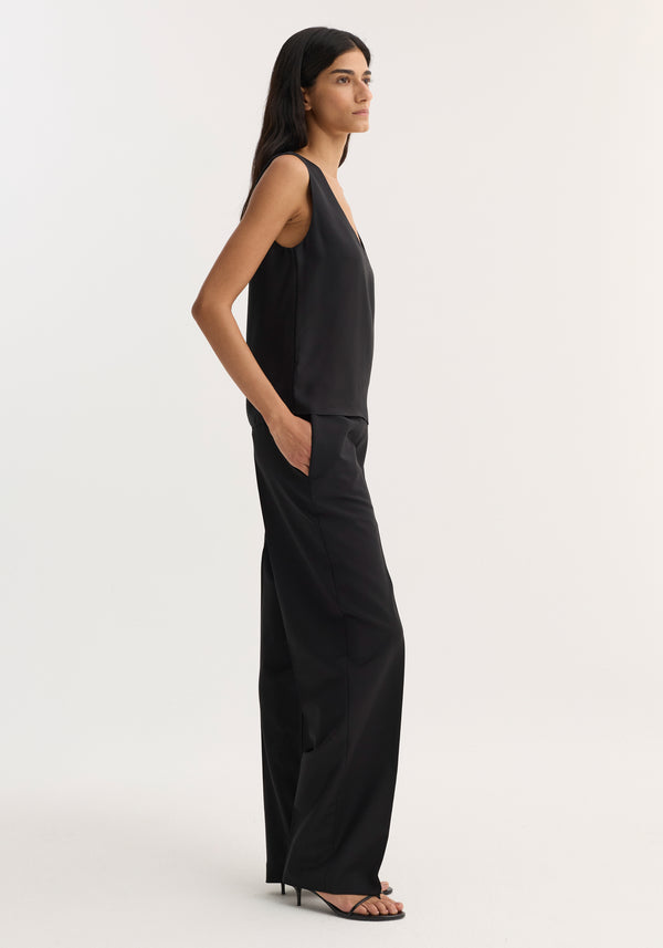 Model wearing a black scoop-neck silk top with a loose fit, paired with wide-leg trousers and open-toe heels, highlighting a minimalist, chic style.