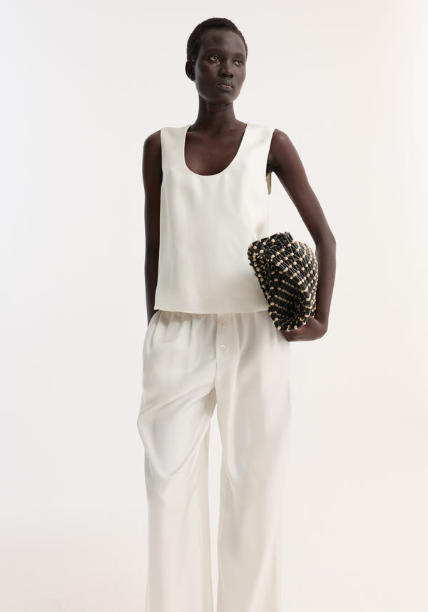 Model wearing Scoop-neck silk top, showcasing its loose fit and wide scoop neck, paired with wide-leg trousers and a woven clutch.