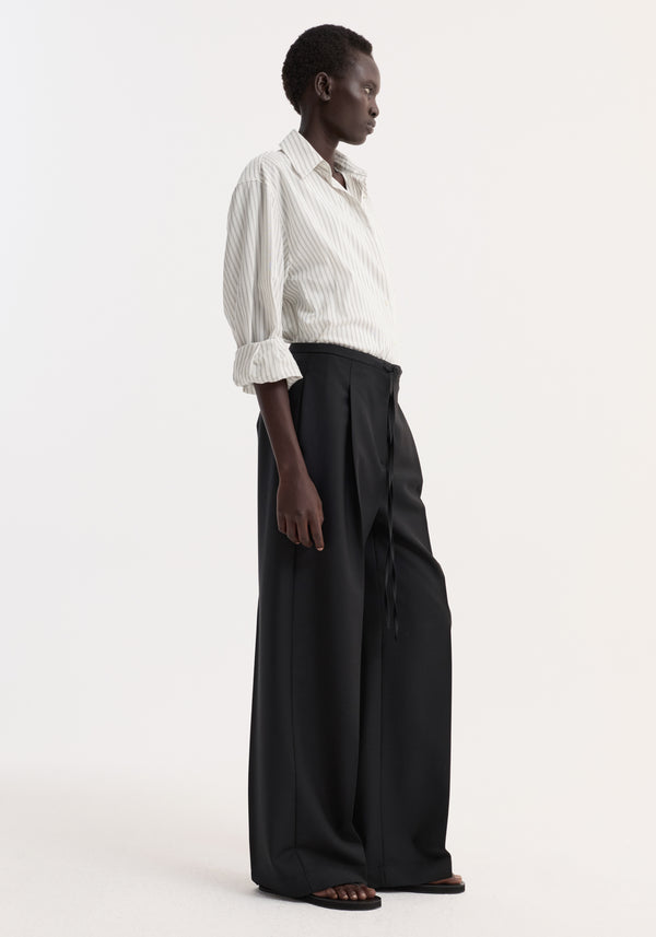 Model wearing Relaxed drawstring trousers in a wide-leg cut with a drawstring waistband, paired with a striped button-up shirt, showcasing an elegant yet casual look.