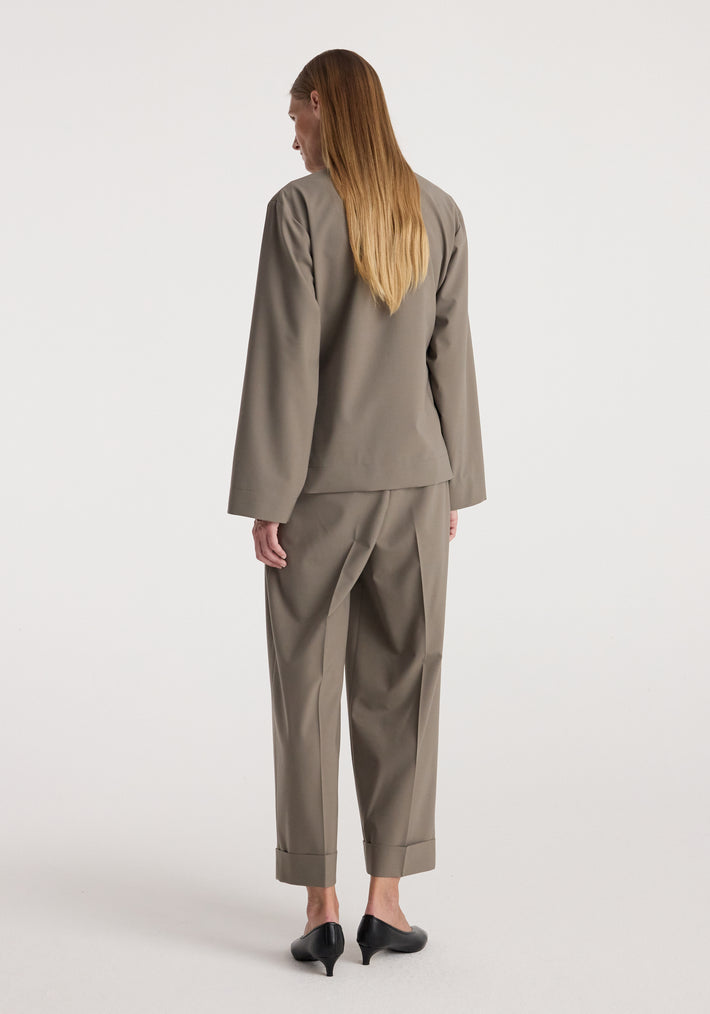 Woman wearing High-waist turn-up trousers | taupe with a matching long-sleeve top and black heeled shoes, standing against a plain light background showing the back view.