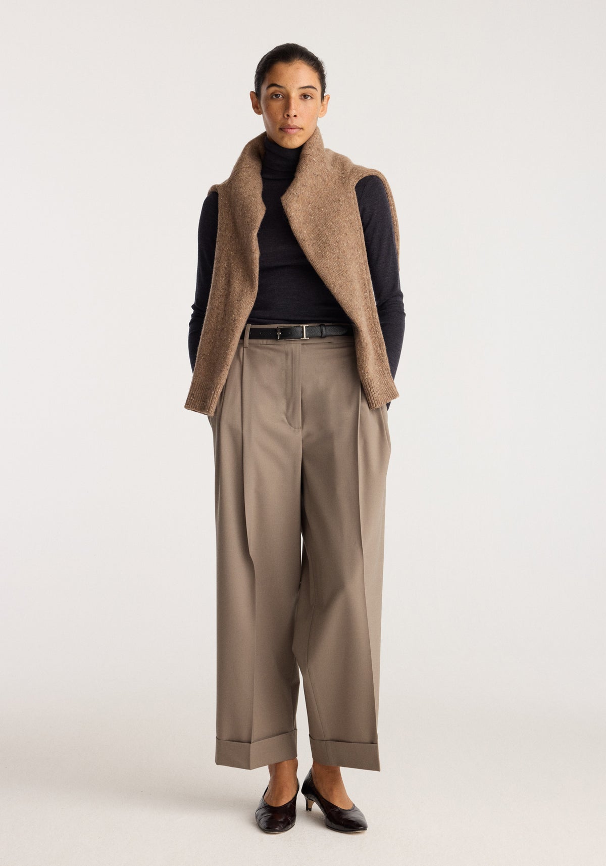 High-waist turn-up trousers | taupe styled on a model with a black top and brown sleeveless vest showing pleated wide legs and turned-up hems