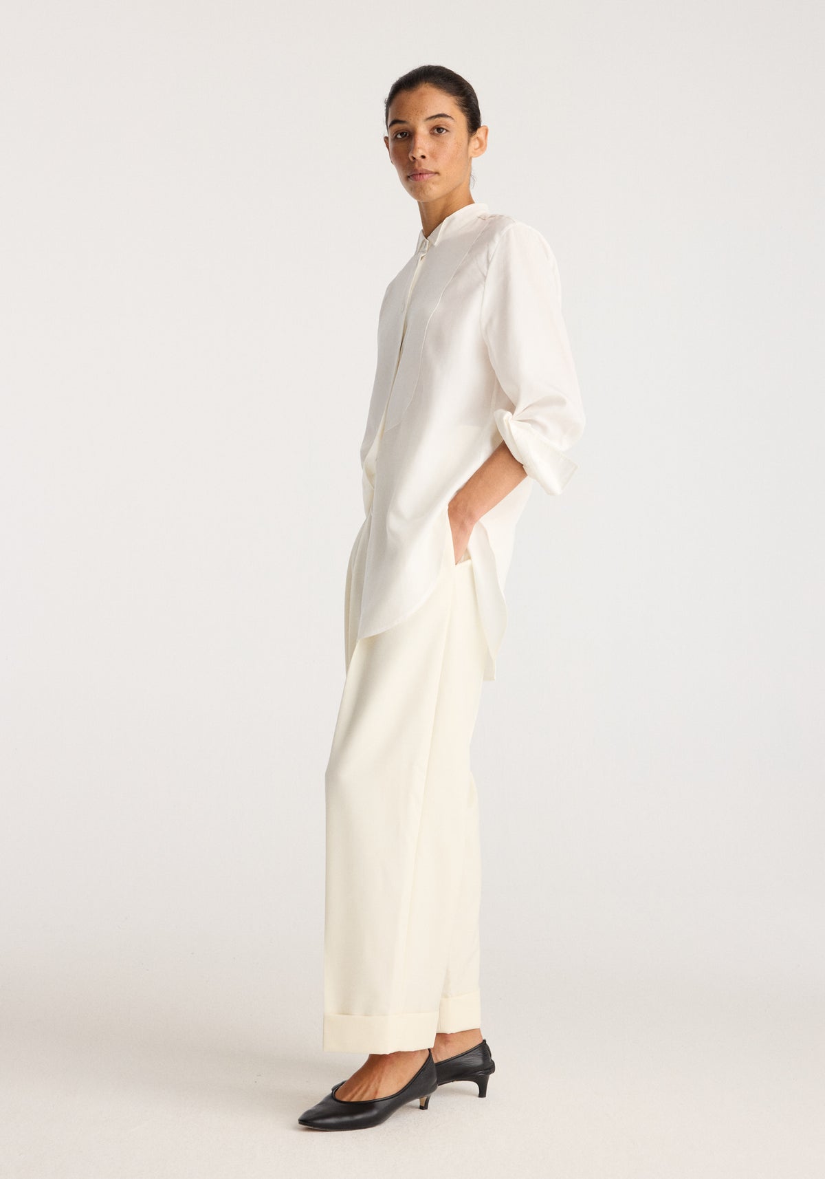Tuxedo shirt | optic white worn by a model with a high collar and relaxed fit paired with wide leg trousers and black heeled shoes