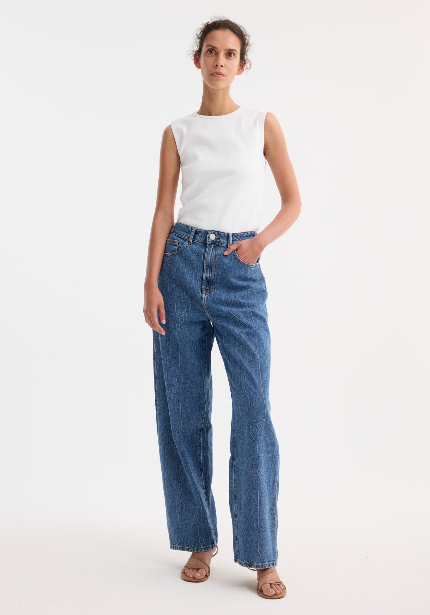 Young woman wearing Signature baggy fit denim, mid denim blue, with a sleeveless ribbed top, showcasing low-waist, wide-leg style, and casual sandals.