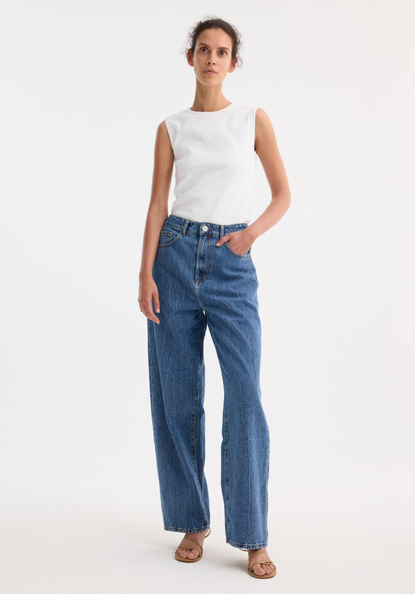 Young woman wearing Signature baggy fit denim, mid denim blue, with a sleeveless ribbed top, showcasing low-waist, wide-leg style, and casual sandals.